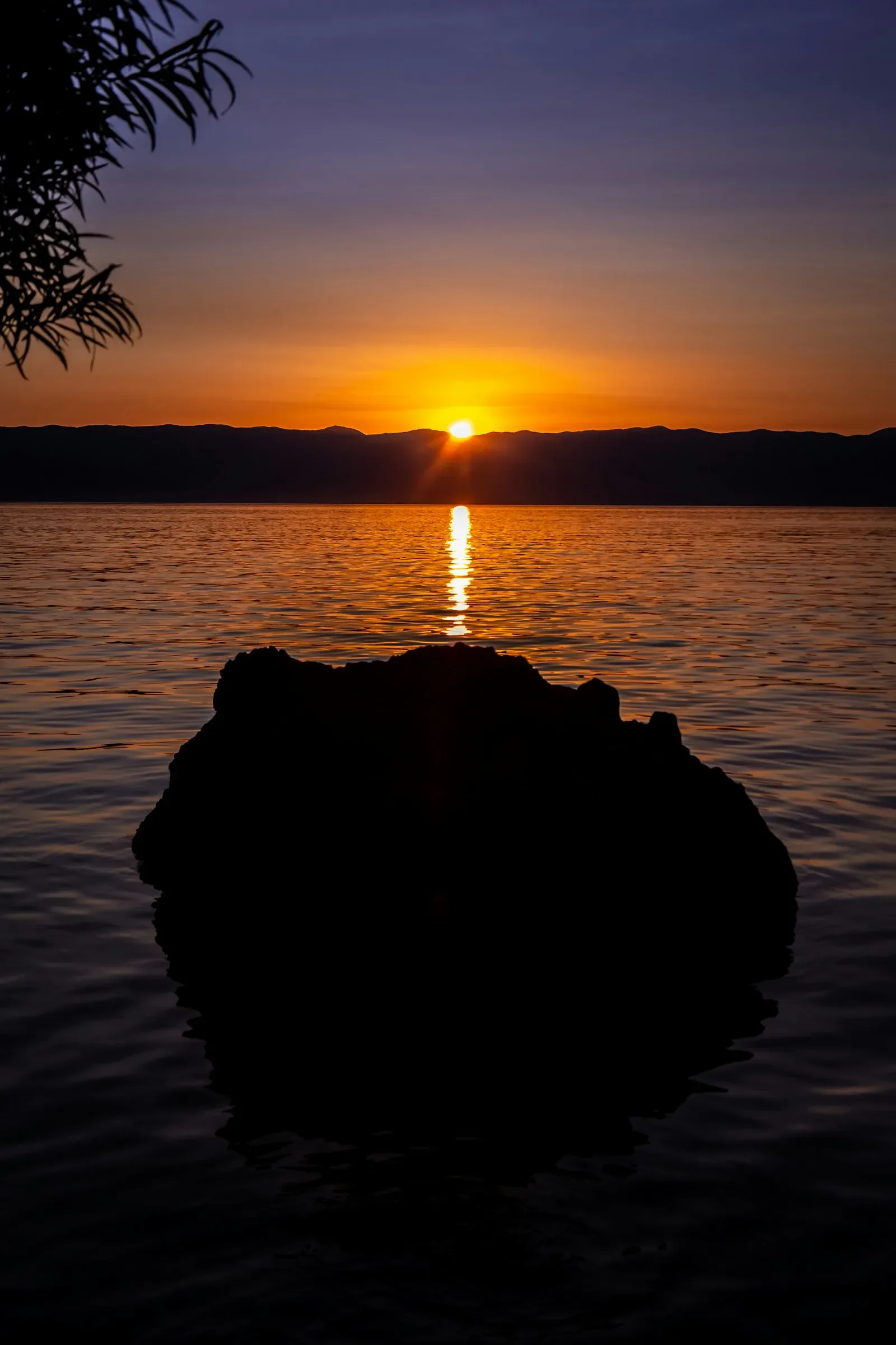 Fels als Silhouette vor dem Sonnenuntergang über einem See